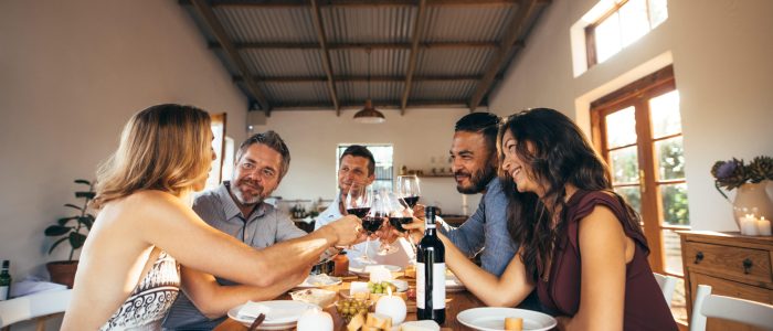 MD4M6W Friends sitting around a table having fun with wine and food. Group of men and women toasting wine at dinner table during party.