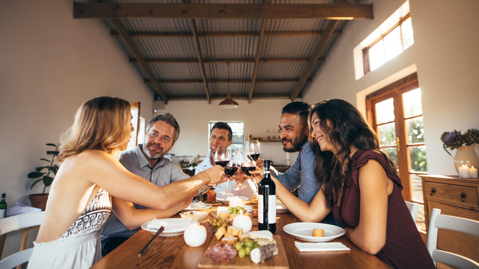 MD4M6W Friends sitting around a table having fun with wine and food. Group of men and women toasting wine at dinner table during party.